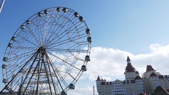 The Ferris Wheel Slowly Rotates in the Amusement Park Against the Background of the Sky