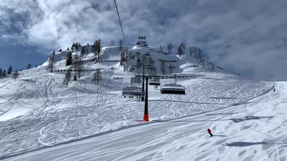 Empty Skilifts Moving On The Ropeway Above Ski Slope In Austrian Alps With People Skiing On The Duri alt