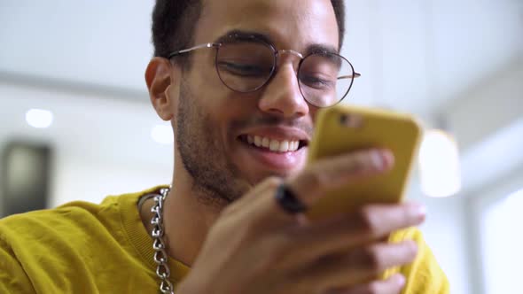 A Young Happy African Man Smiles and Texts on His Smartphone alt