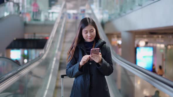 Pretty traveler female use smartphones while using escalator at airport