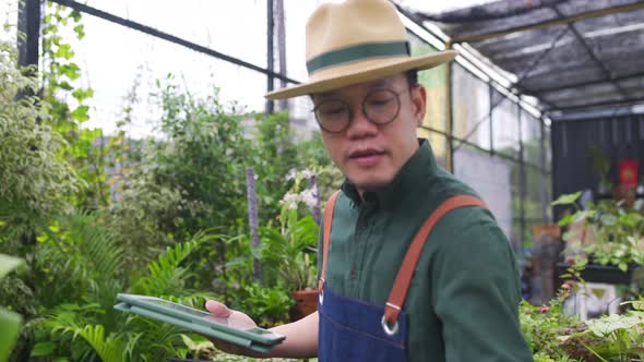 4K Asian man plant shop owner caring plants and flowers in greenhouse garden. alt