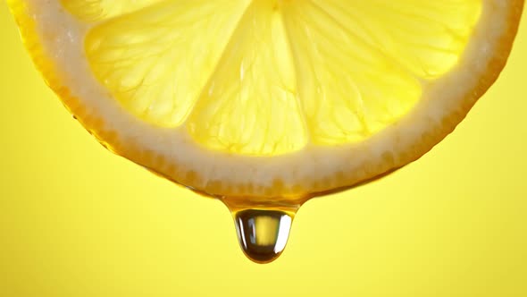 Super Slow Motion Macro Shot of Water Drop Falling From Lemon Slice on Yellow Background at 1000Fps alt