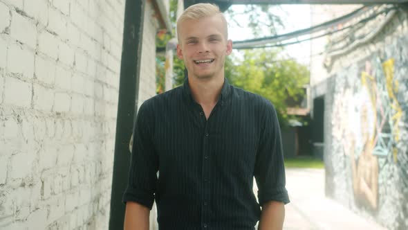 Slow Motion Portrait of Cheerful Young Man Showing Okay Hand Gesture and Smiling Standing Outdoors alt