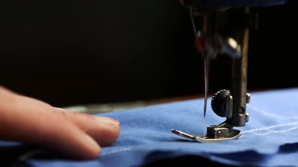 Seamstress Sews With A White Thread On A Sewing Machine A Blue Fabric Close Up