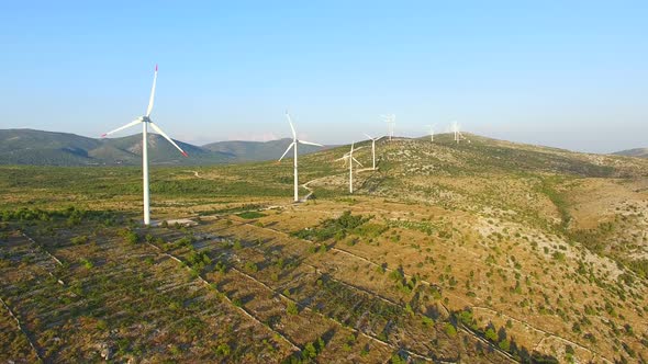 Flying above a group of white wind turbines with red tip blades on a sunny day alt