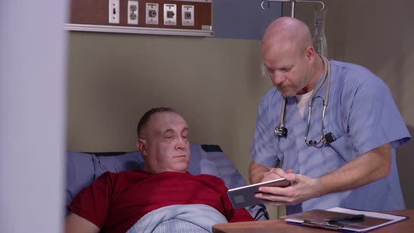 Male nurse looks at digital tablet with senior man in hospital bed