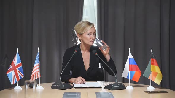 Middleaged Blonde Caucasian Political Leader Drinks Water During a Press Conference