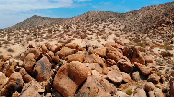 A Man stands on a Mountain made of Rocks looking out over a barren desert in Joshua Tree on his own, alt