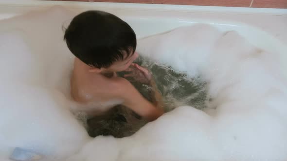 Boy 6-7 Years Sitting in the Bubble Bath, Playing, Smiling. View Top.