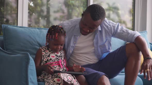 African American father and daughter playing in living room, Kid girl and dad playing on a tablet