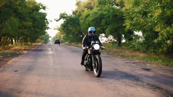 Front View of a Man in Grey Helmet and Leather Jacket and Plaid Shirt Riding Motorcycle on an alt