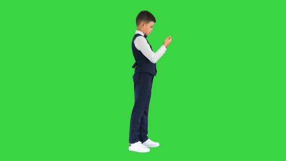 Little Boy in Waistcoat Watching Something on His Phone and Rounding His Eyes in Shock on a Green alt
