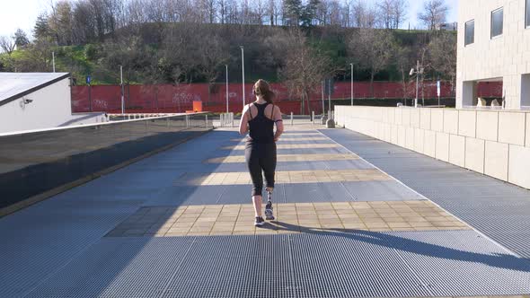 Slow motion shot of jogging woman with leg prosthesis in the city alt