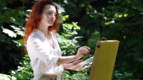 Middle Aged Redhead Woman With an Easel in The Forest
