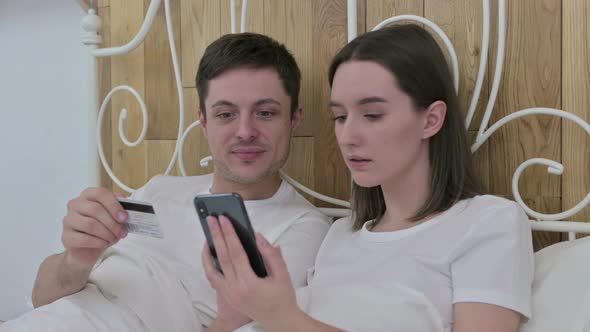 Young Couple Making Online Payment on Smartphone in Bed  alt