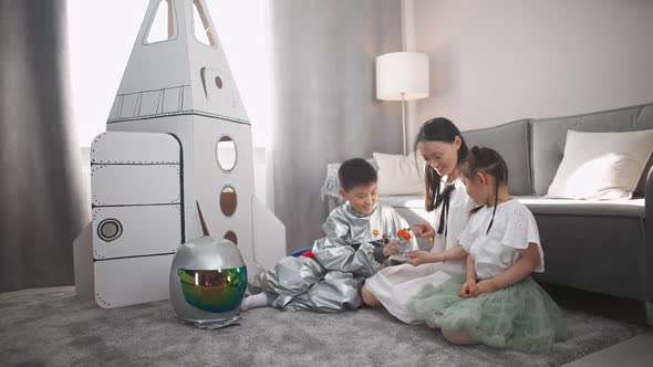 Asian Female with Kids Play in the Living Room at Home a Boy in an Astronaut Costume Sitting on the alt