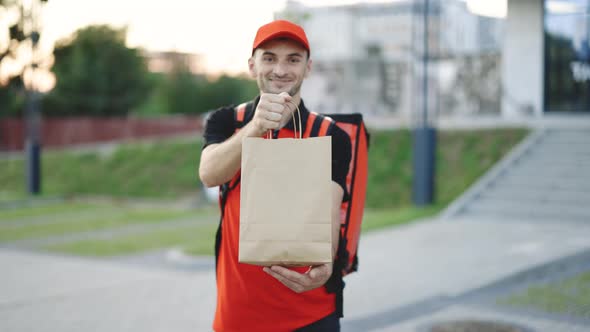 Outdoor Portrait of Delivery Man With Red Uniform Holding Food Bags Waiting for Customer