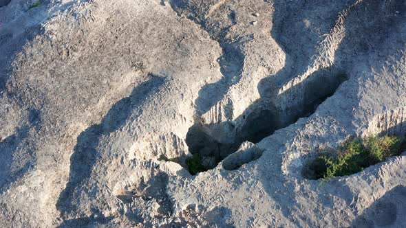 Erosion of bare wrinkled rock with holes - texture of a rough stone with furrowed surface alt