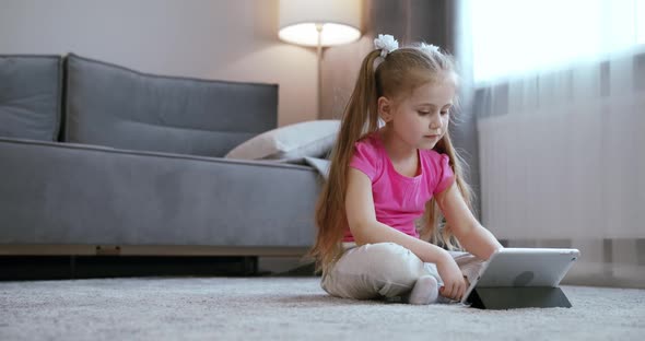 Curious Cute Preschool Kid Girl Using Digital Tablet Technology Device Lying on Carpet Floor Alone alt