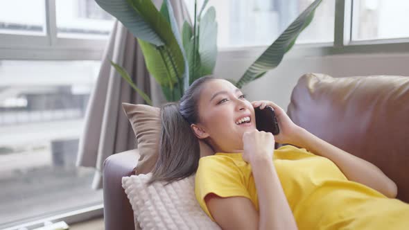 Asian woman on the phone talking on the sofa happily and smiling.