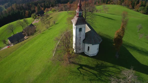 Aerial View of Hills, Colorful Forest and Sv Tomaz Church. Sunset in Slovenia in Autumn