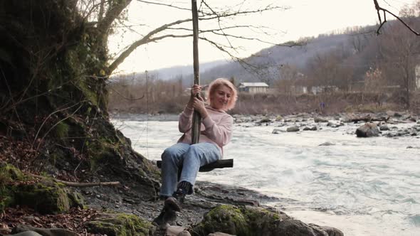 Happy young woman smiling and swinging on nature by the river