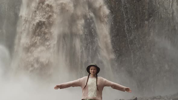 Woman traveler in hat stands and raises her hands up near Karakaya-Su waterfall, nature, slow motion