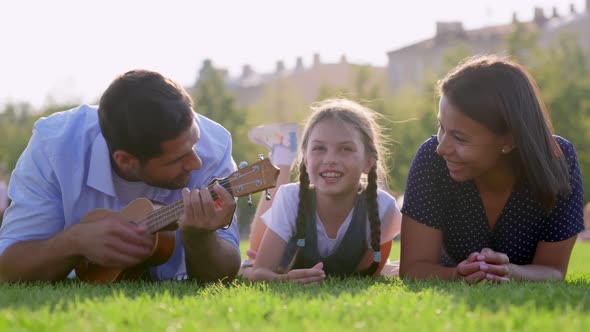 Portrait of Multiethnic Family Lying on Green Lawn in Park Playing Ukulele alt