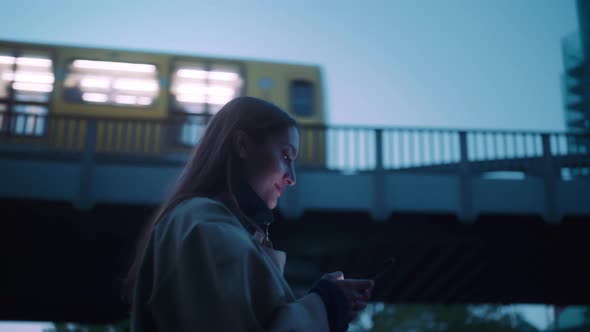 Young woman smiling and walking while blurry metro goes in the background alt