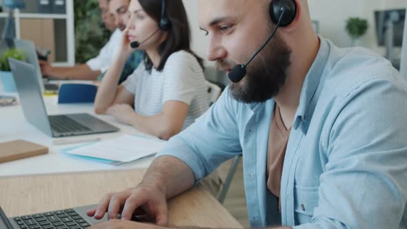 Male Customer Service Specialist Speaking and Typing Using Laptop in Modern Office alt