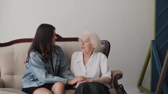 Young Girl Caresses Grandmother's Hands During Pleasant Conversation in Room alt