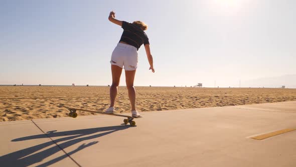 Rear View Of A Sporty Woman Riding Skateboard In Skatepark On Desert Landscape - wide, slow motion alt