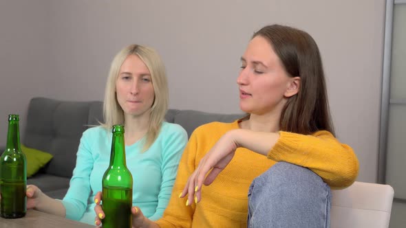 Two girls, drinking beer and eating delicious pizza, at home in their kitchen. alt