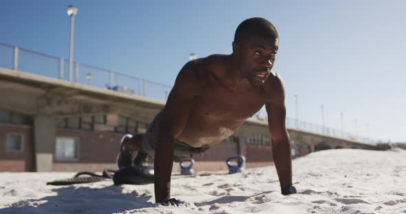 Focused african american man doing press ups, exercising outdoors on beach alt