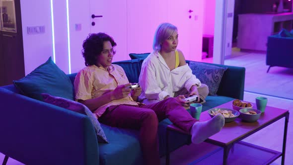 Happy Young People Playing Video Games on Console While Sitting on Couch in Front of Tv. Millennial alt