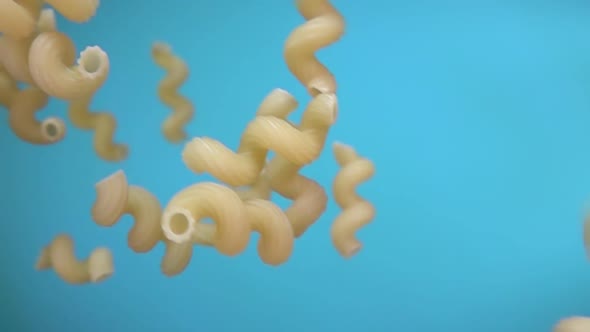 Close-up of Dry Pasta Cellentani Falling Diagonally on the Blue Background alt