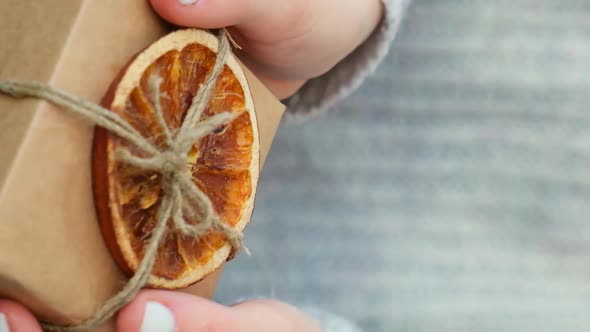Woman Giving Box with New Year's Gifts Wrapped in Craft Paper and Decorated with Dry Orange Slices alt