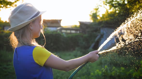 Funny Little Girl in Hat Playing with Garden Hose in Sunny Backyard. Adorable Little Girl Playing alt