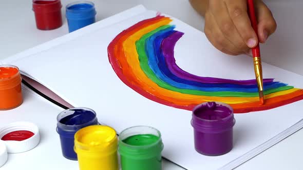 The girl draws a rainbow on paper with multicolored paints. Drawing with the eyes of a child.