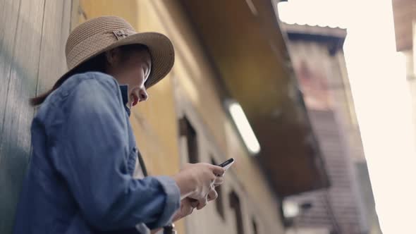 Asian female using smartphone typing scrolling new feed social media at a small street.