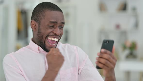 Portrait of African Man Celebrating Success on Smartphone  alt