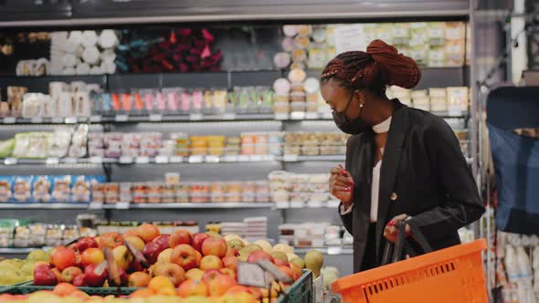 African American Young Woman in Medical Mask Choosing Apple Fruit Vegetable in Supermarket alt