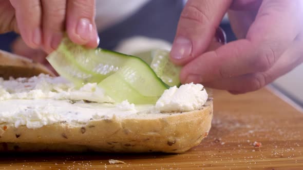 chef puts thin slices of fresh cucumber on crunchy bun prepare cheese sandwich alt