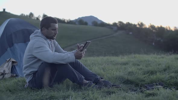 Young Man Using Tablet in Nature Mountain Outdoor at Sunrise or Sunset Slow Motion alt