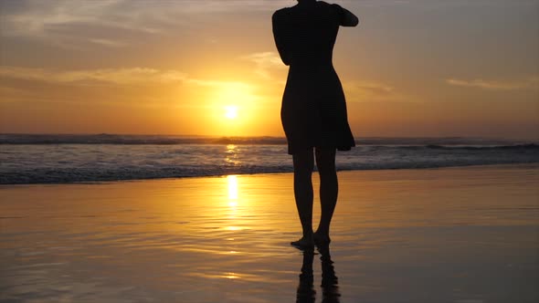 A young woman walks on the beach at sunset. alt