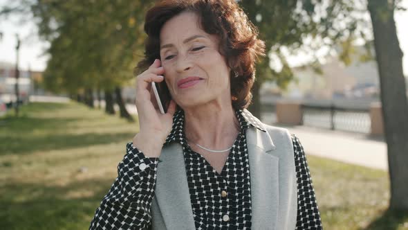 Cheerful Senior Woman Making Mobile Phone Call Talking and Smiling Outdoors alt