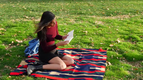 A female college student reading a book and relaxing outdoors in the park with autumn leaves and gre alt