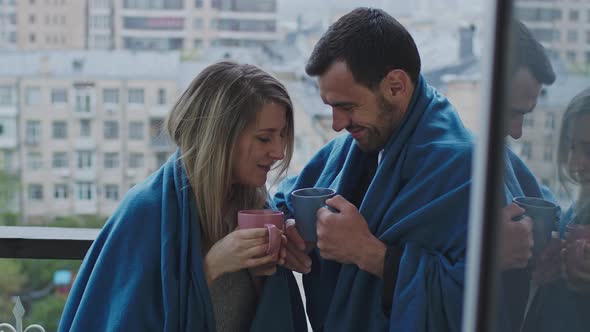 Man and Women Stand on the Balcony with Plaid and with Mugs alt