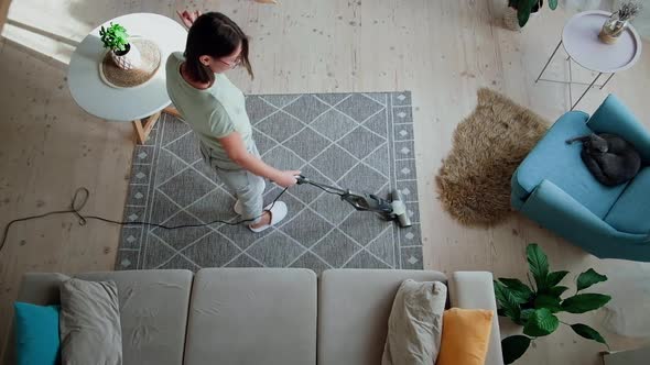 Young Woman Cleaning the Carpet with a Vertical Vacuum Cleaner Dancing and Fun at Home While alt
