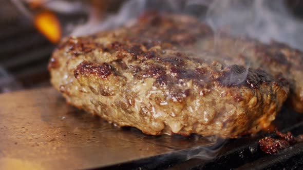 Slow motion of beef hamburger on a grill in close up with flames and smoke alt